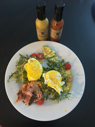 eggs benedict and salmon on arugala, avocado, and tomato with hot sauce