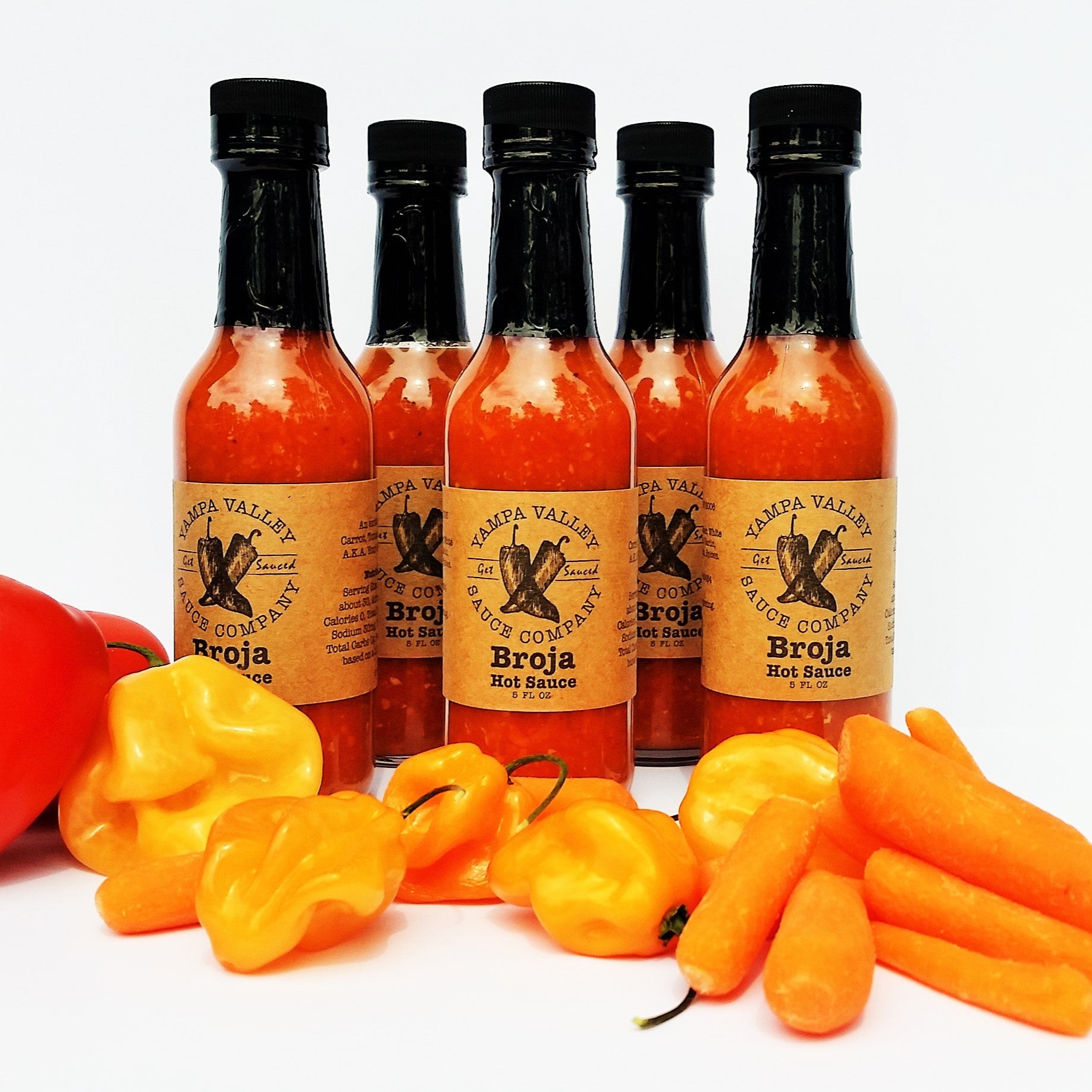 Set of hot sauce bottles with hanabero peppers and carrots on a white background