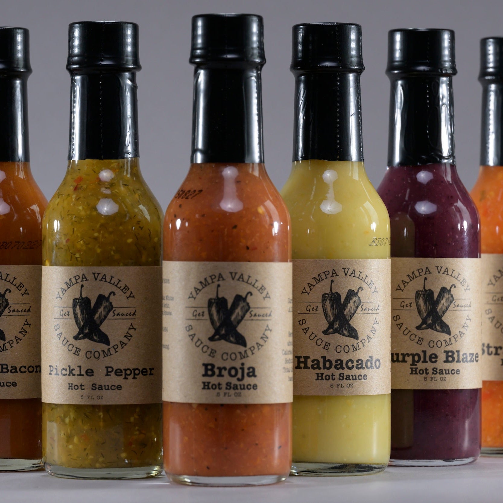 Row of naturally flavored hot sauce bottles with labels on a gray background