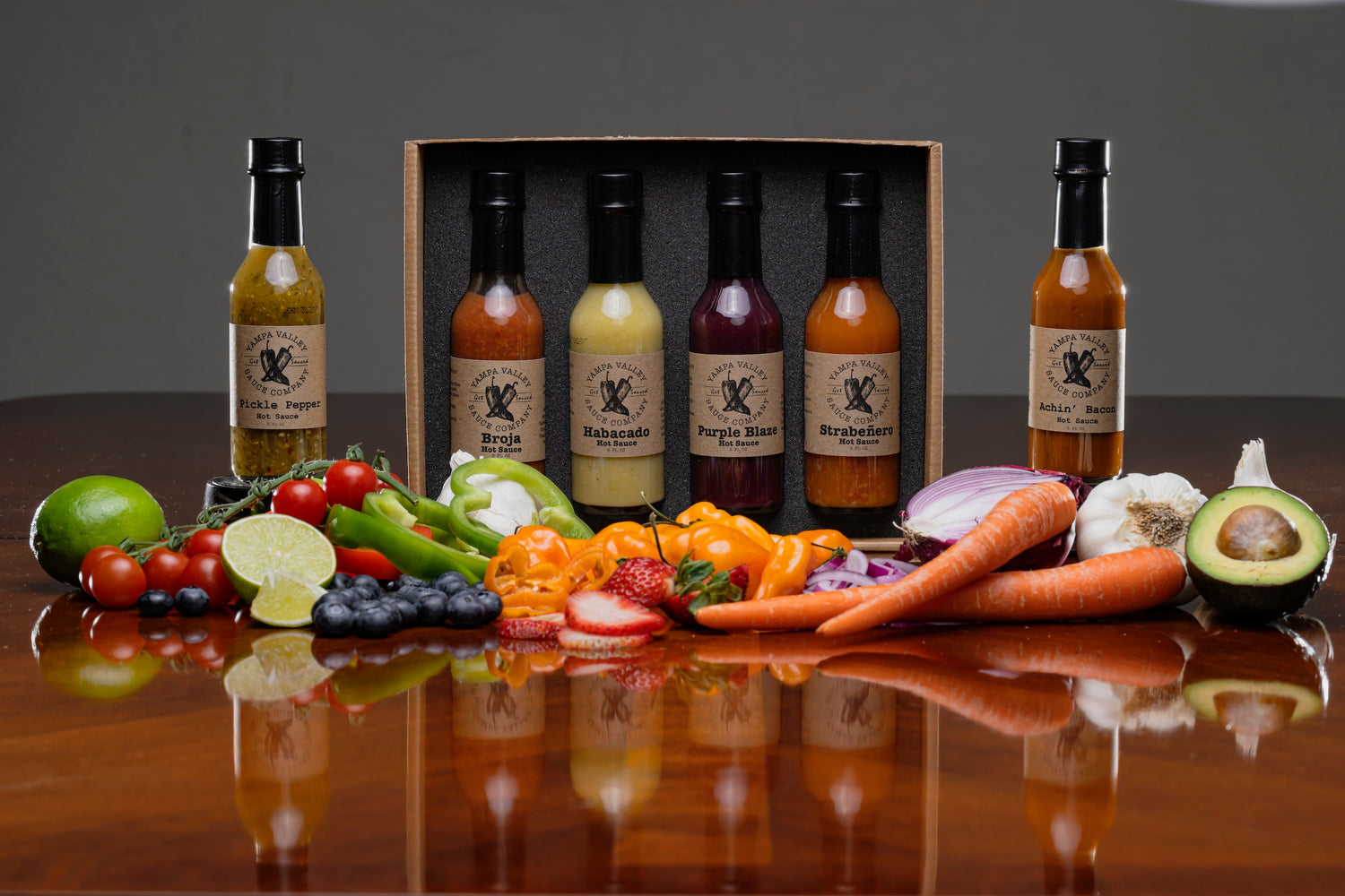 Hot Sauces lined up in front of a pile of fresh ingredients like carrots, onions, and other fruits and vegetables